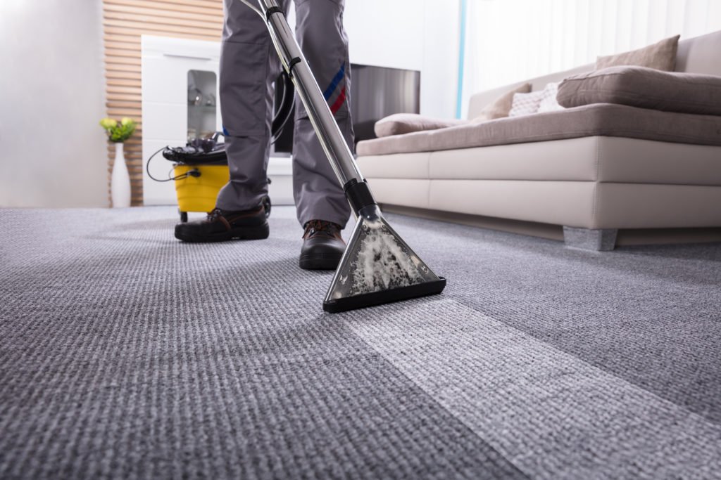 low section of a person cleaning the carpet with vacuum cleaner